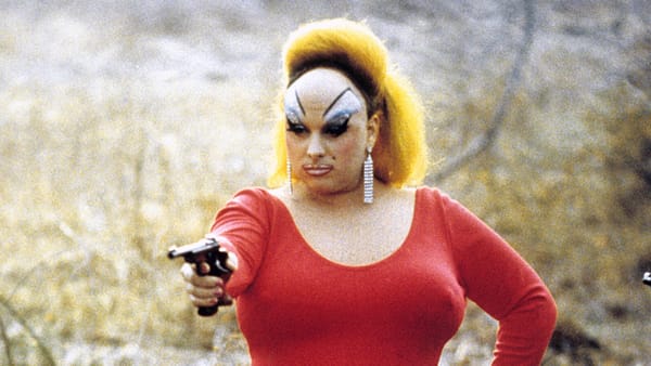 Divine, star of the film Pink Flamingos, holds a gun while wearing a red dress. 