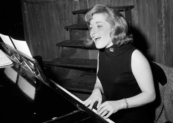 A black and white photo of Lesley Gore, singing behind a piano